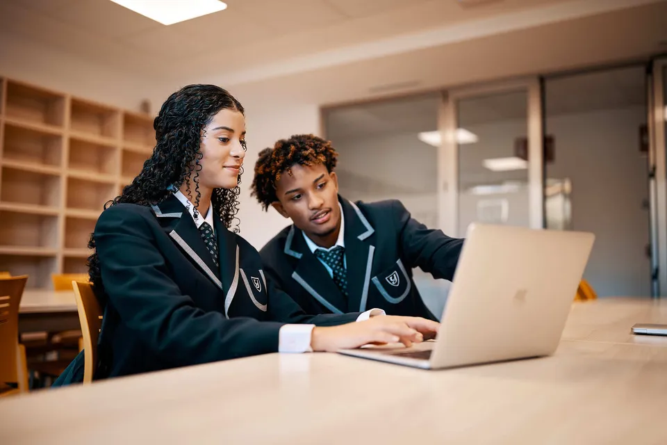 Due studenti della Yago School lavorano concentrati al laptop in un'area con librerie.