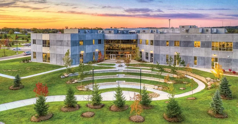 L'edificio moderno della South Christian High School si trova in un'area verde esterna con un percorso circolare sotto un cielo serale variopinto.