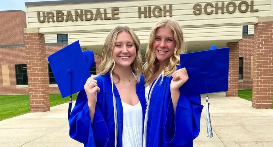 Due studentesse in toga da diploma blu sono davanti all'edificio in mattoni della Urbandale High School.
