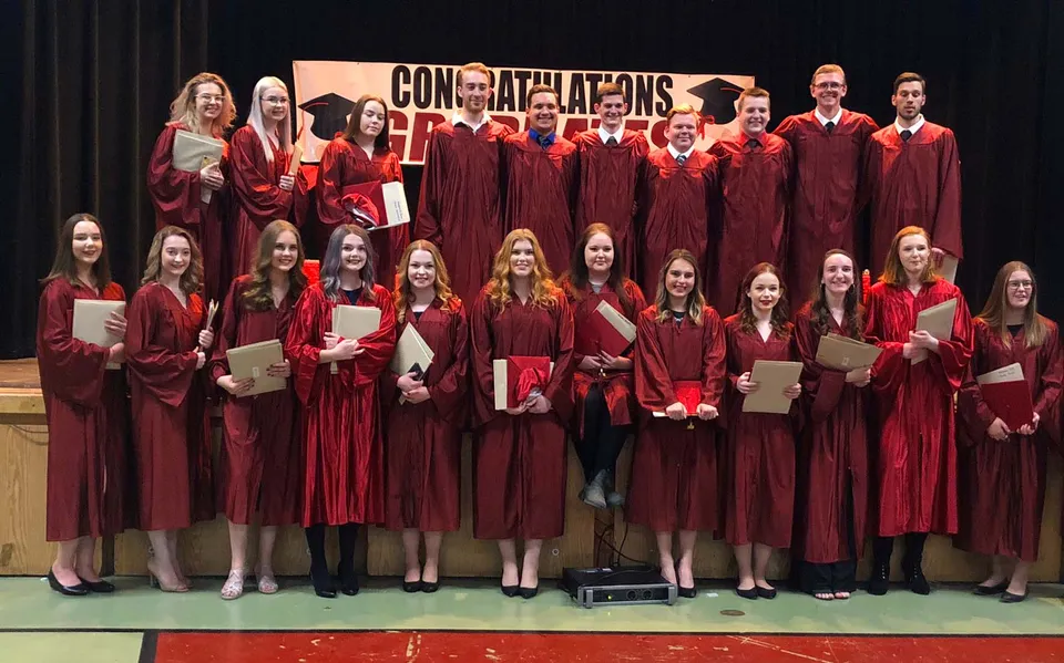 Un gruppo di diplomati della Carbonear Collegiate High School indossa toghe rosse su un palco con uno striscione con la scritta 'Congratulations'.