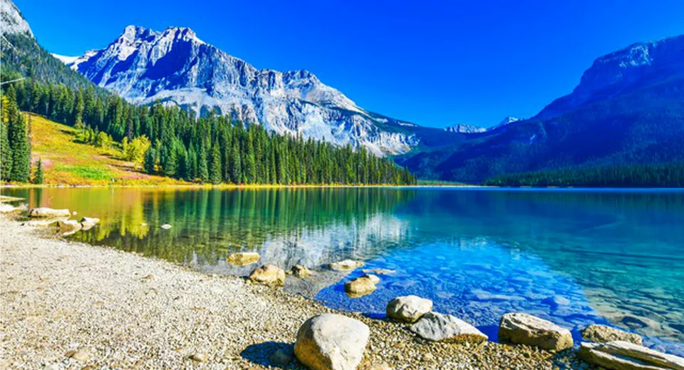 Un tranquillo lago alpino con montagne innevate e una sponda boscosa nelle vicinanze della John Barsby Secondary School.