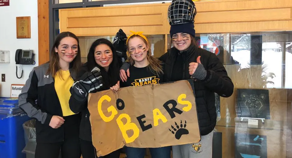 Quattro studentesse stanno davanti a un edificio della Banff Community High School tenendo un cartello con la scritta 'Go Bears'.
