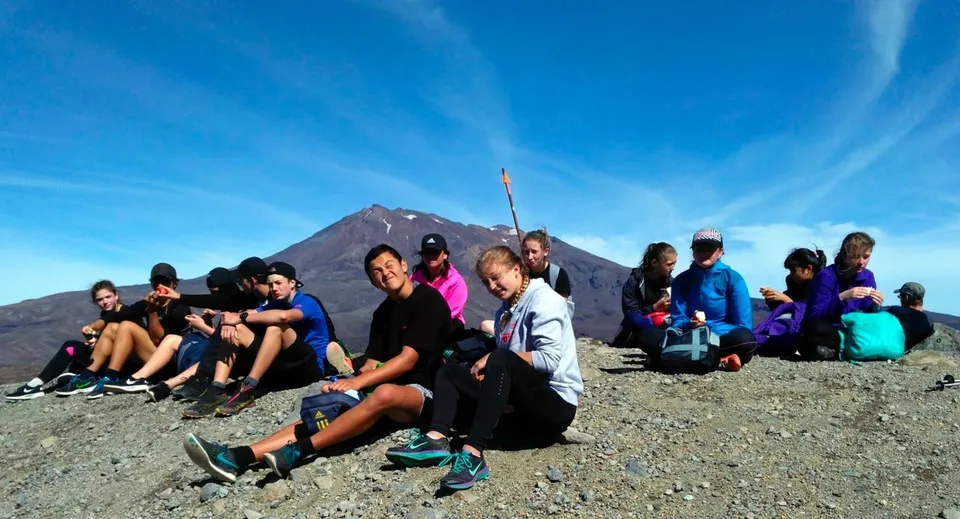 Un gruppo di studenti della Taumarunui High School siede davanti a una montagna innevata sotto un cielo blu.