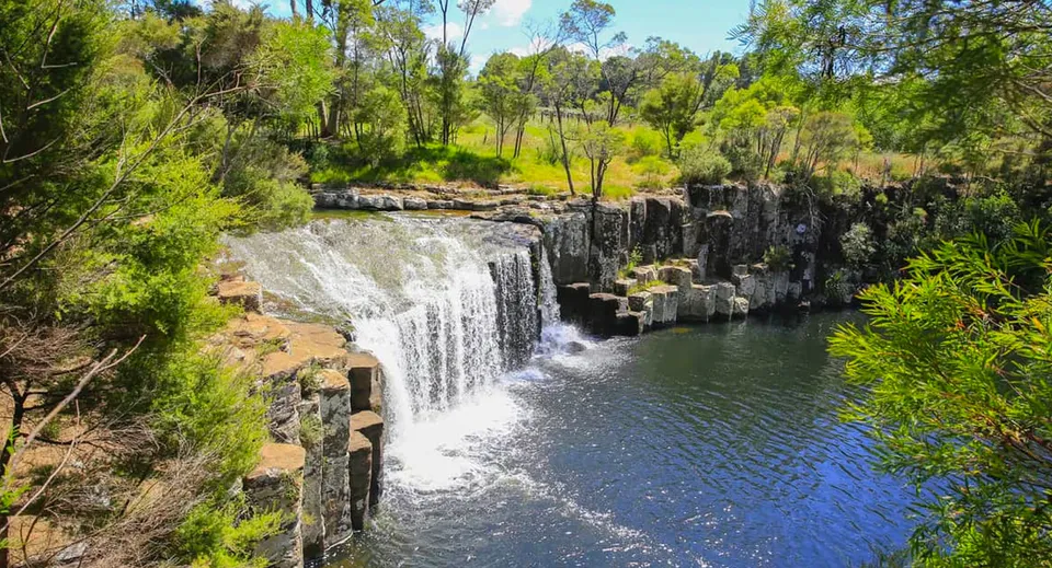 Una cascata scorre sulle rocce in una piscina naturale blu, circondata dalla natura verde, vicino alla Springbank School.
