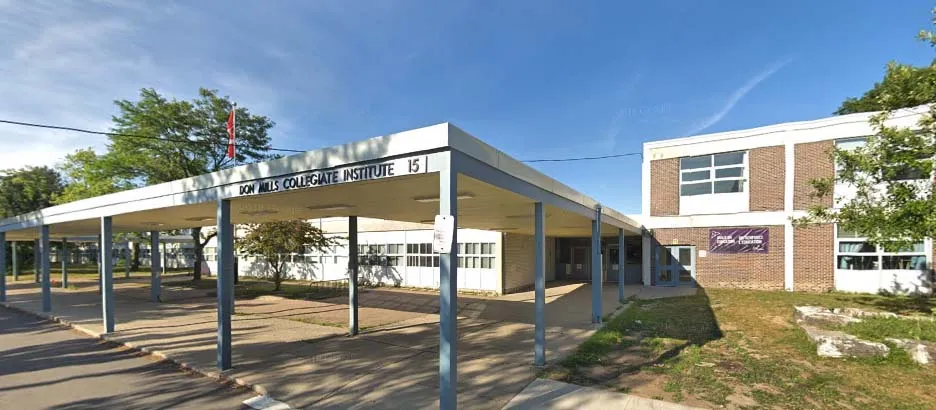 El edificio moderno de varios pisos del Don Mills Collegiate Institute con un camino cubierto y rodeado de árboles bajo un cielo despejado.