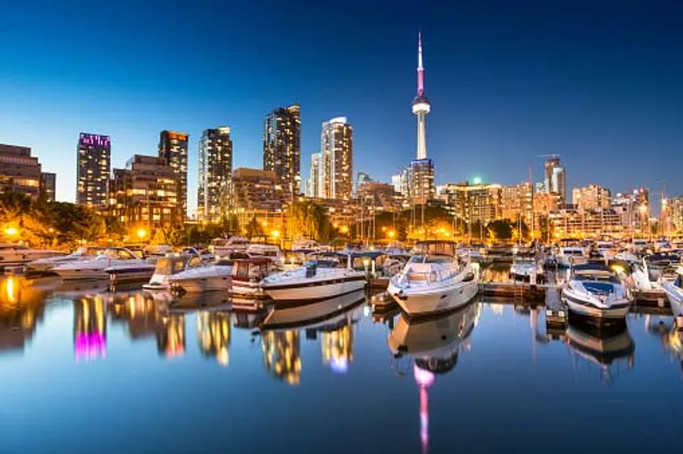 Lo skyline illuminato di Toronto con la CN Tower e diverse barche nel porto al tramonto.