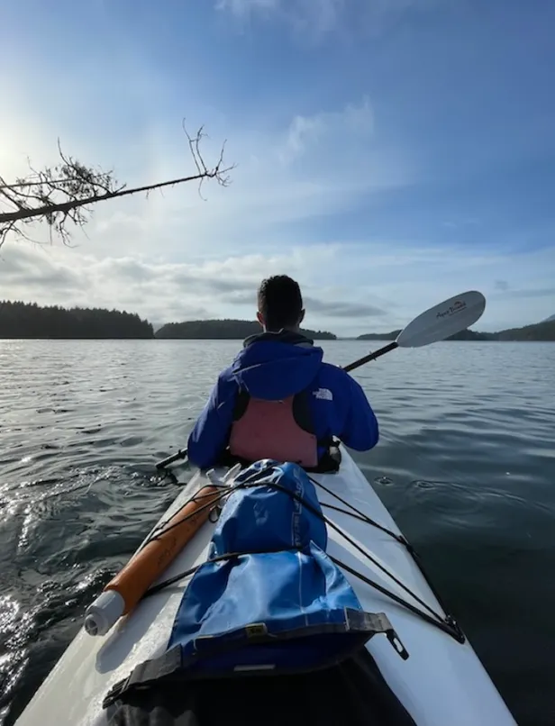 Vista desde un kayak de un joven remando en un lago rodeado de bosque