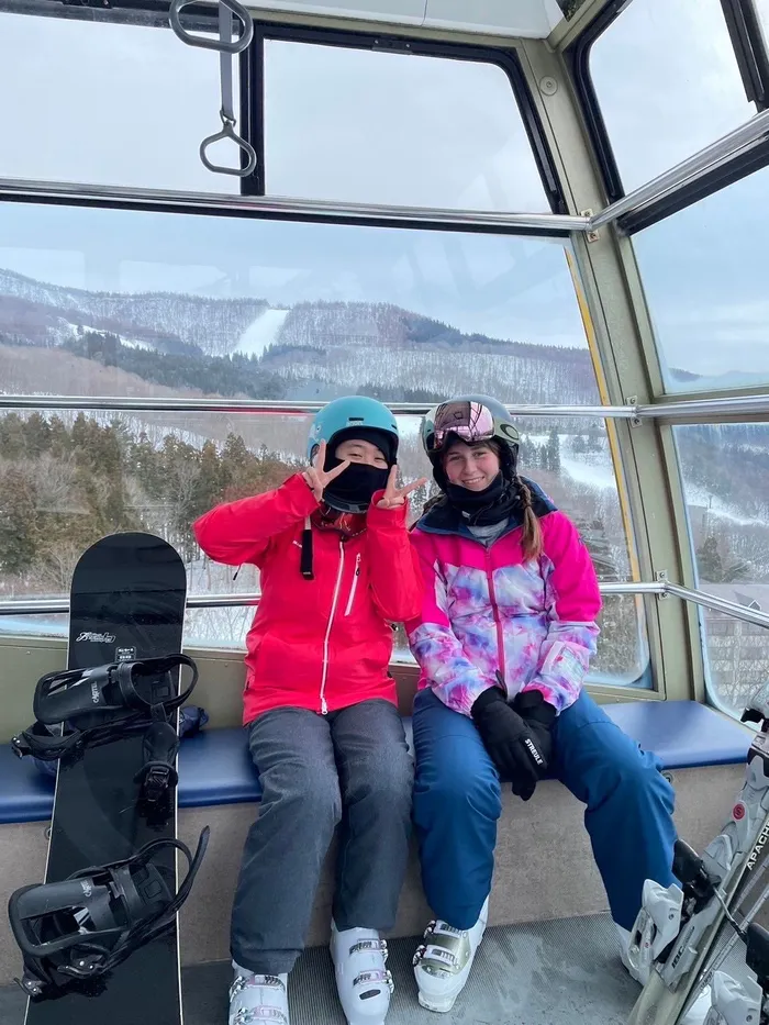 Due ragazze in tenuta da sci in una cabinovia con snowboard, montagne innevate sullo sfondo