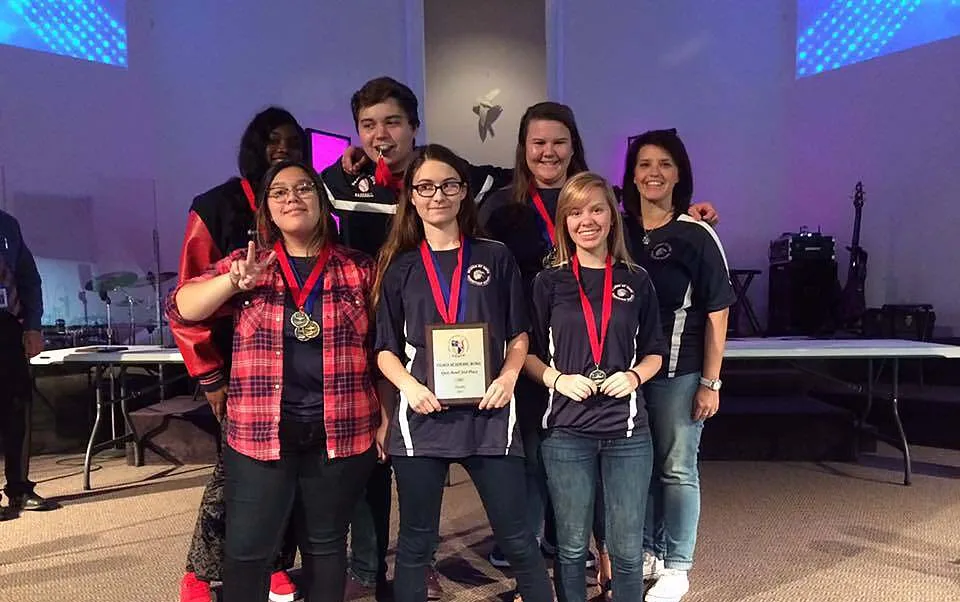 Un gruppo di studentesse e studenti della Beacon of Hope Christian School si trova sul palco con strumenti musicali e impianto luci sullo sfondo.
