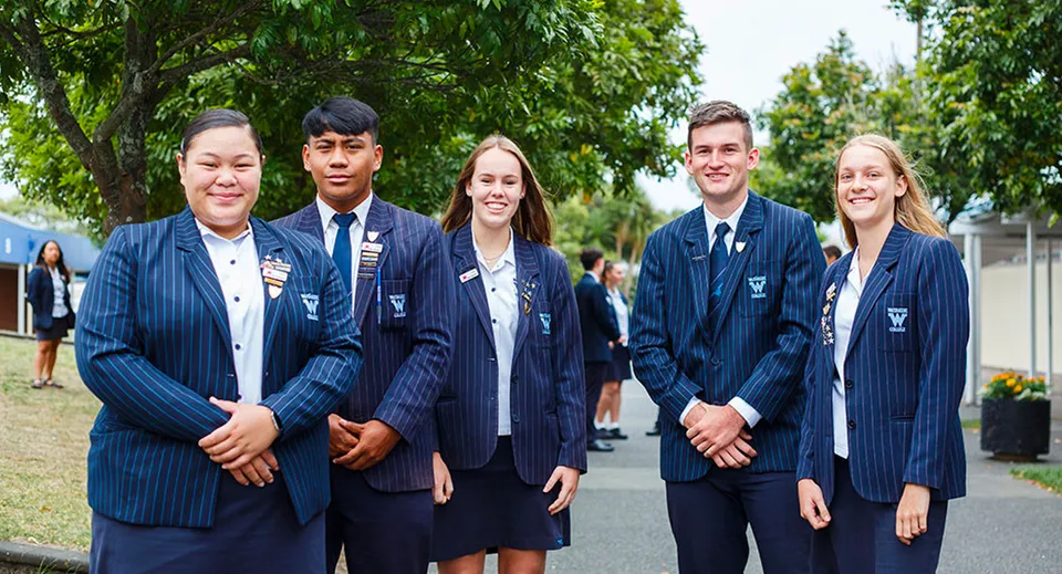 Un gruppo di studenti e studentesse in uniforme si trova insieme nell'area verde all'aperto del campus del Waitakere College.