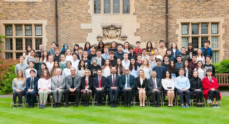 Un gruppo di studenti si trova in piedi e seduto davanti a un edificio in mattoni nel campus di MPW Cambridge.