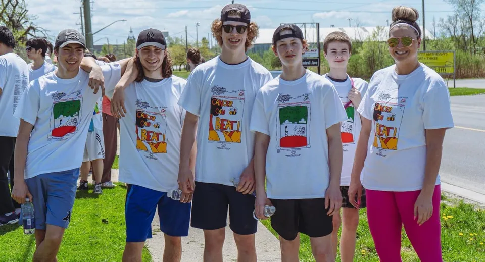 Un gruppo di studentesse e studenti della Fort Erie International Academy sta insieme all'aperto su un prato con alberi sullo sfondo.