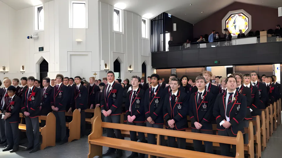 Studenti del St. Bede's College sono seduti in un'aula simile a una chiesa con dettagli architettonici decorati.