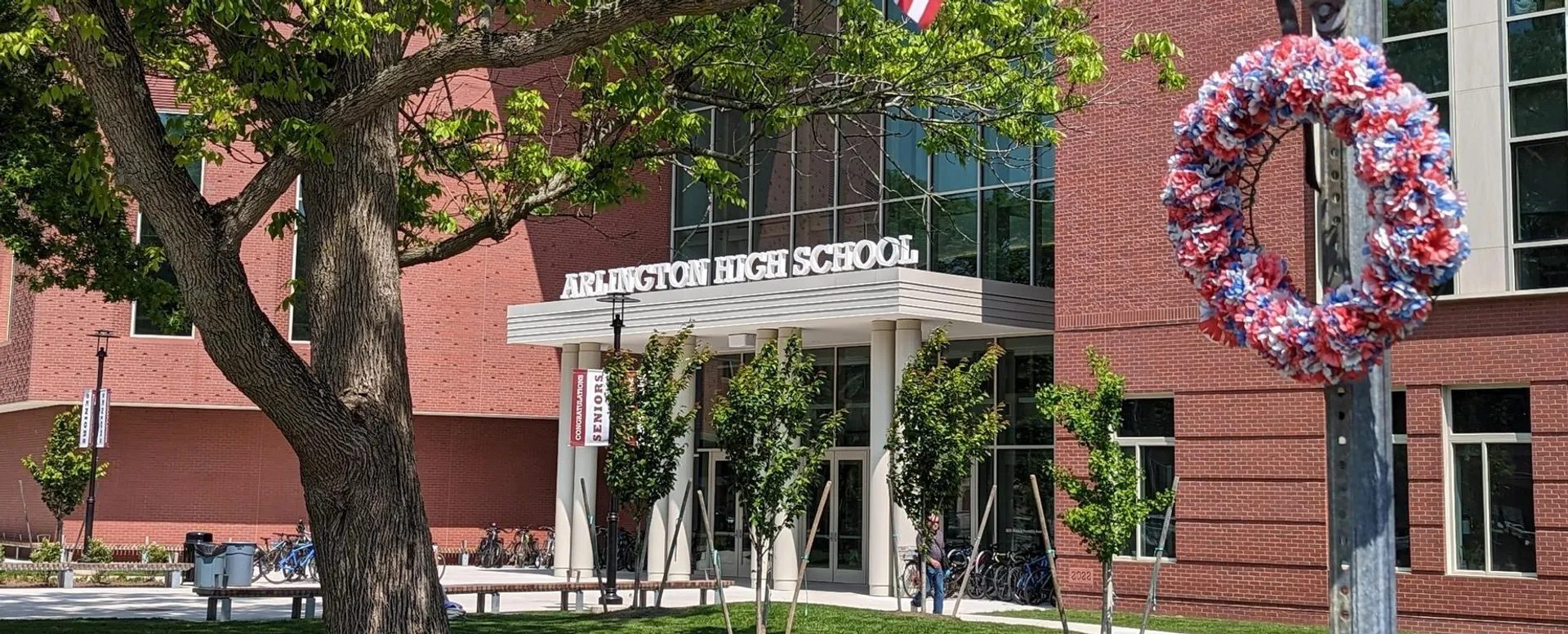 L'edificio in mattoni della Arlington High School è circondato da una verde vegetazione e mostra un banner colorato in primo piano.