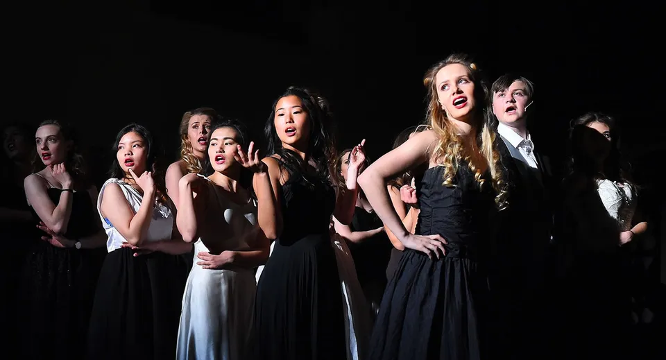 Un gruppo di studentesse dell'Epsom College mette in scena uno spettacolo teatrale su un palco al buio.