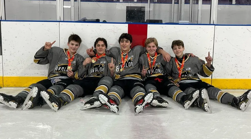 Un gruppo di giovani giocatori di hockey siede in divisa sul ghiaccio della pista della Holy Spirit High School.