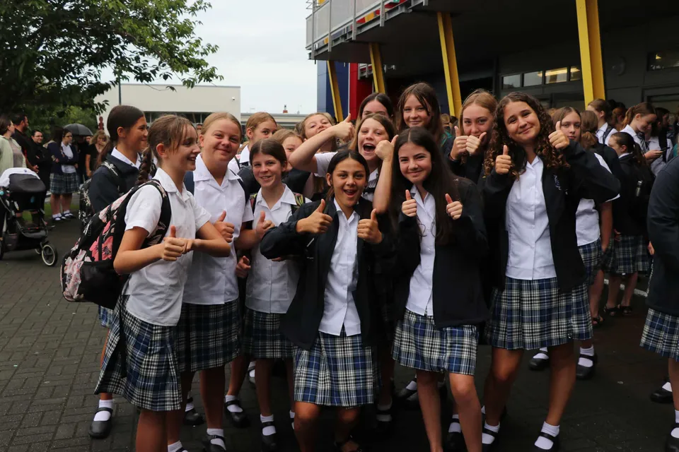 Un gruppo di studentesse della Napier Girls' High School posa su un marciapiede facendo il gesto del pollice in su.