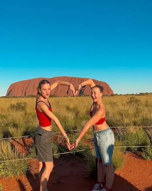 Due studentesse formano un cuore con le braccia davanti a Uluru, nell'outback australiano