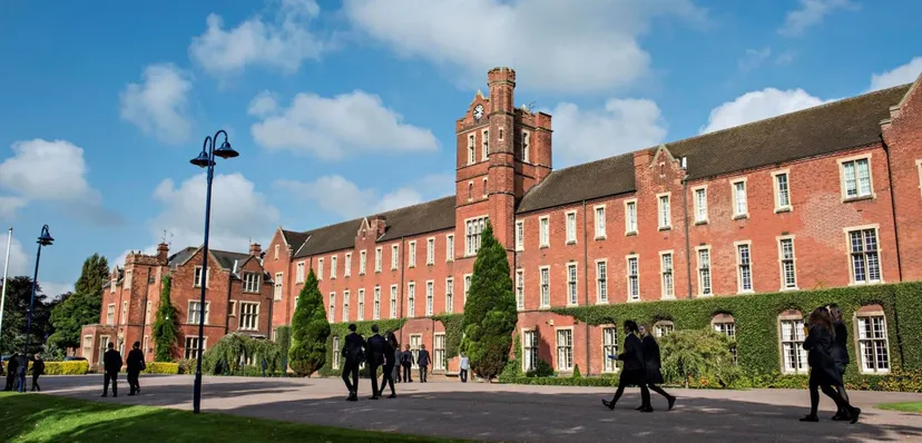 L'edificio storico in mattoni rossi del Trent College con una torre dell'orologio e studenti nel piazzale.