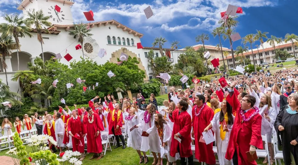 I diplomati della Bishop Garcia Diego High School si riuniscono davanti a un edificio con palme sotto un cielo azzurro.