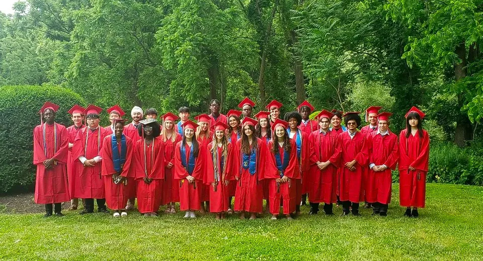 Un gruppo di diplomati della The Knox School si trova all'aperto circondato da alberi verdi.