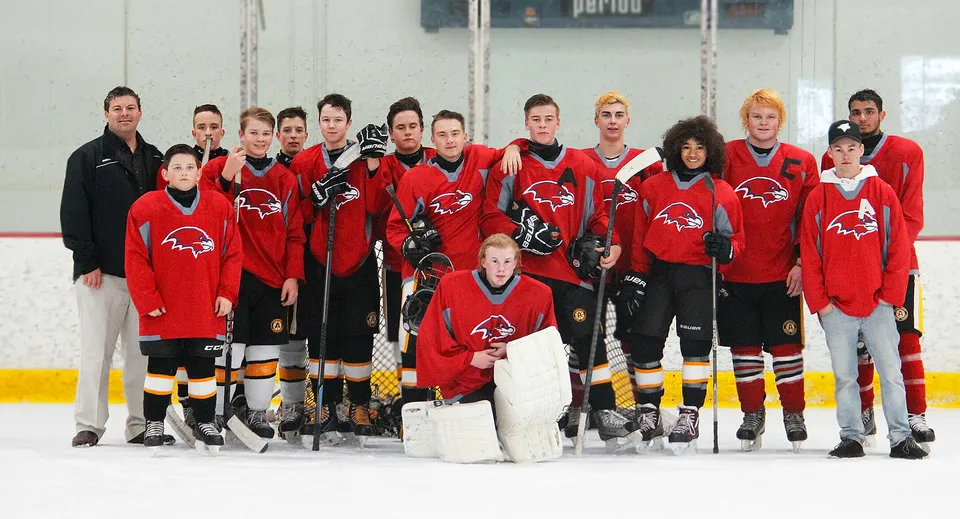 Studenti della D.W. Poppy Secondary School con maglie rosse e nere su una pista da ghiaccio durante una partita di hockey.