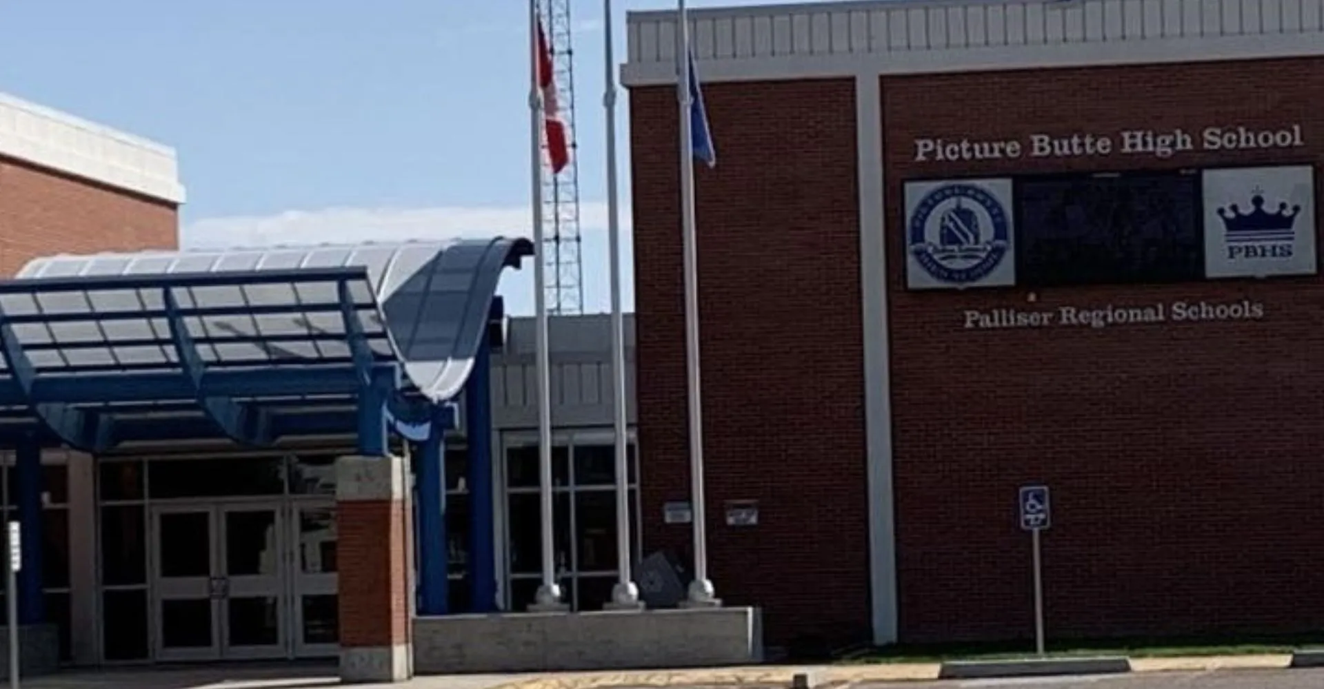 Si vede l'edificio in mattoni della Picture Butte High School con l'ingresso caratteristico e le bandiere al vento.
