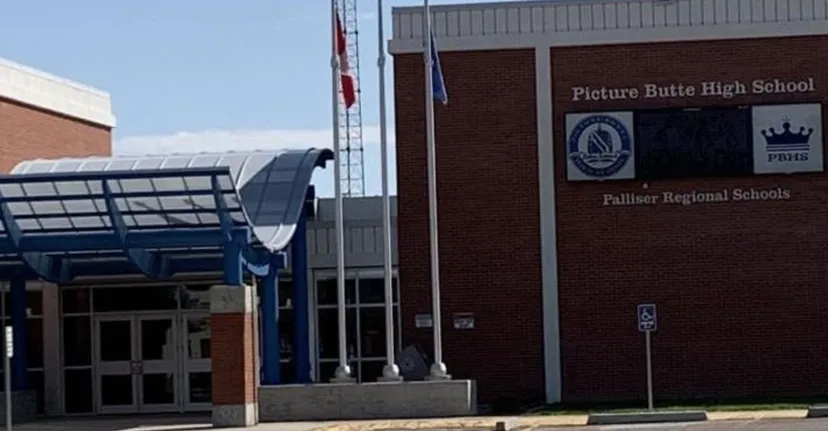 Si vede l'edificio in mattoni della Picture Butte High School con l'ingresso caratteristico e le bandiere al vento.
