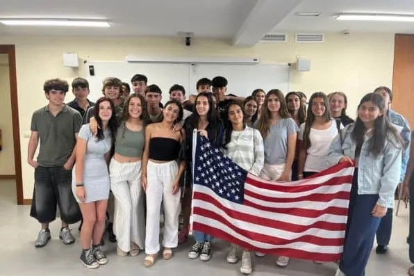 Grupo de estudiantes en un aula posando juntos y sosteniendo una bandera de Estados Unidos