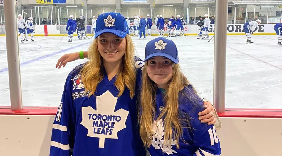 Due studentesse della Gravenhurst High School indossano maglie dei Toronto Maple Leafs e posano davanti a un'arena di hockey su ghiaccio.