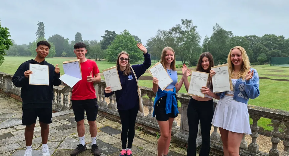 Studenti della Sherfield School sono all'aperto e tengono in mano i loro certificati davanti a un paesaggio verde.