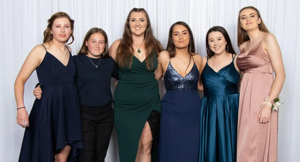 Un gruppo di sei studentesse in diversi abiti da sera nel campus dell'Aotea College davanti a uno sfondo bianco.