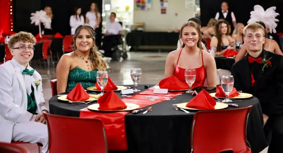 Studenti e ospiti della Wellington High School sono seduti in abito formale a una tavola imbandita a festa con tovaglie rosse e nere.