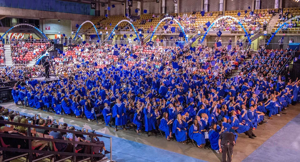 I neodiplomati della Ross Sheppard High School indossano toghe blu durante la loro cerimonia di diploma in un'aula magna affollata.