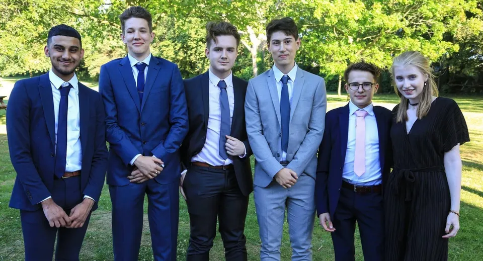 Un gruppo di sei persone in abito formale è insieme nel parco nei terreni della Kingham Hill School.