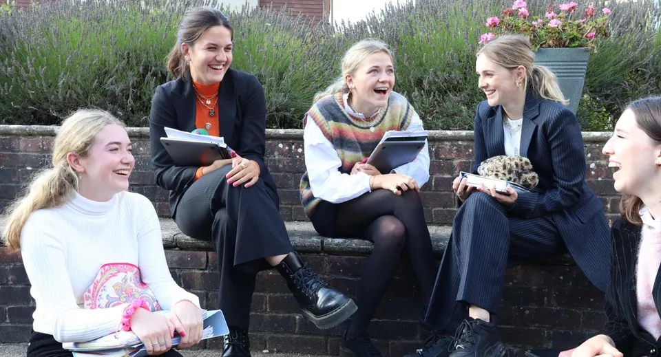 Quattro studentesse della Godolphin School sono sedute su un muretto e chiacchierano immerse nel verde.