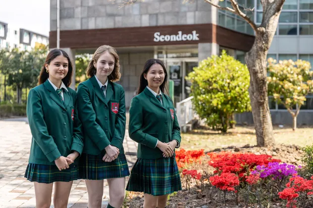 Drei Schülerinnen in grüner Schuluniform vor dem Schulgebäude in Korea