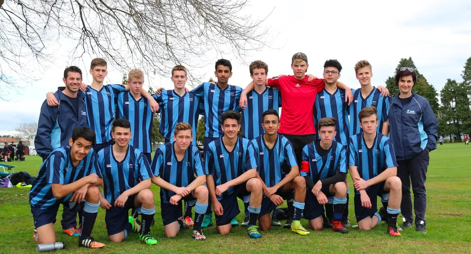 Un gruppo di giovani calciatrici e calciatori della ACG Strathallan è in piedi insieme su un campo erboso con alberi spogli sullo sfondo.