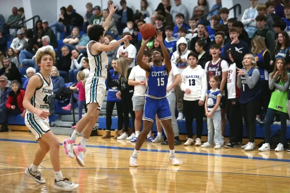 Studenti giocano una partita di basket sul campo della Cotter Schools con spettatori sugli spalti.