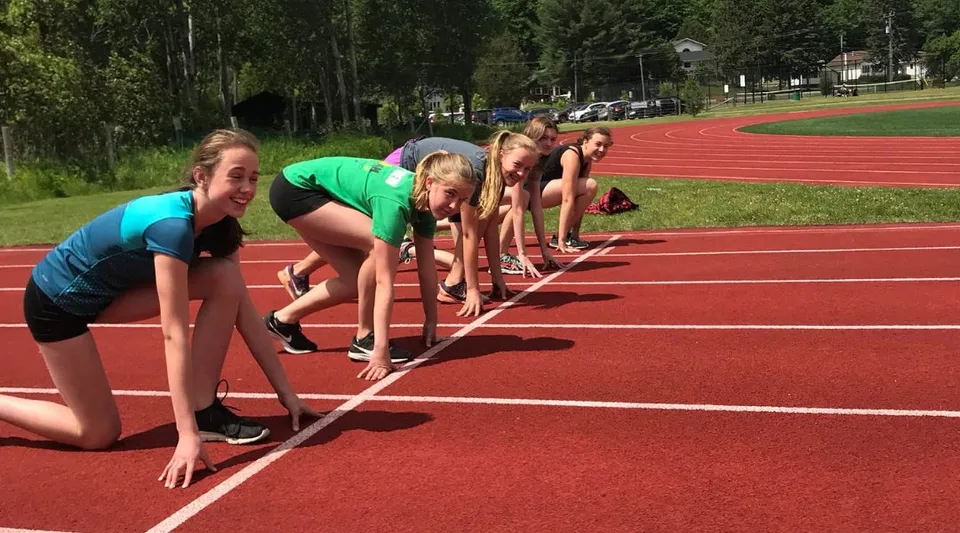 Cinque studentesse della Huntsville High School in posizione di partenza sulla pista di atletica rossa.