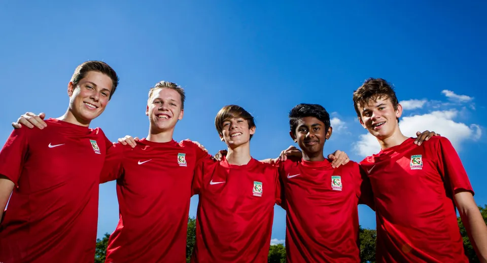 Un gruppo di cinque studenti in maglia da calcio rossa si trova davanti a un cielo blu nel campus del Kelvin Grove State College.