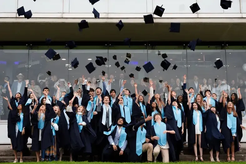 Estudiantes de Nord Anglia International School Dublin lanzan sus birretes al aire vestidos con togas de graduación.
