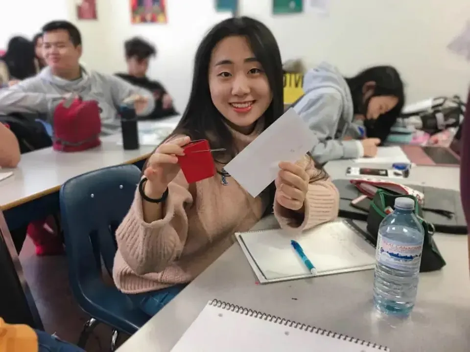Una studentessa della Urban International High School siede sorridente alla scrivania e tiene in mano una busta rossa in un'aula.
