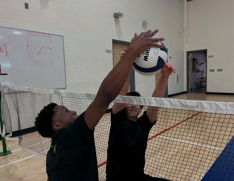 Una persona in maglietta nera gioca a pallavolo sul campo sportivo della École secondaire publique Maurice Lapointe.