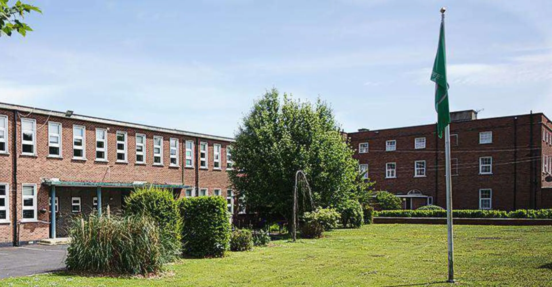 Si vede il cortile interno verde della Manor House School con edifici in mattoni e un alto pennone.