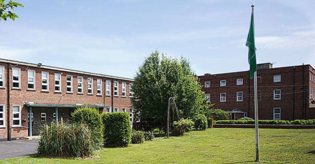 Si vede il cortile interno verde della Manor House School con edifici in mattoni e un alto pennone.