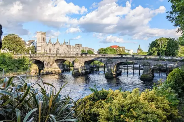 Antico ponte di pietra ad archi su un fiume con edifici storici, in Irlanda