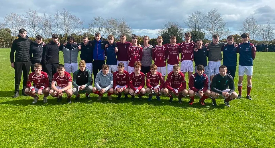 Un gruppo di studenti della St. Ciarán’s Community School posa insieme su un campo sportivo con alberi e un cielo nuvoloso sullo sfondo.