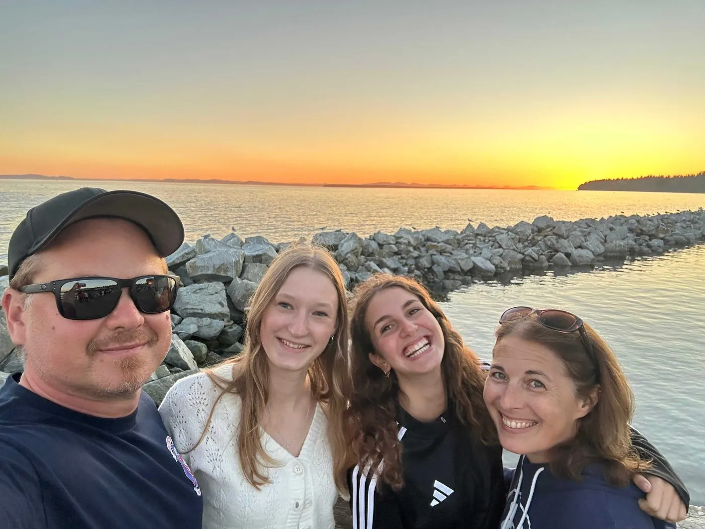Gastvater, zwei Gastschülerinnen und Gastmutter beim Selfie am Meer im Sonnenuntergang