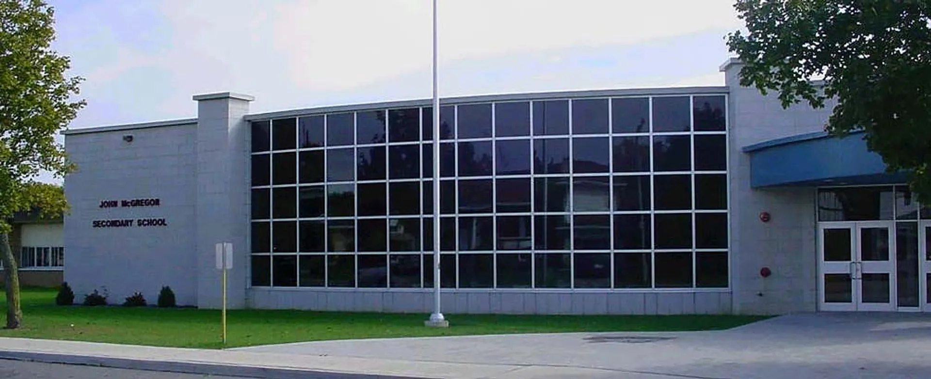 L'edificio moderno a più piani della John McGregor Secondary School sorge su un'area verde con alberi.